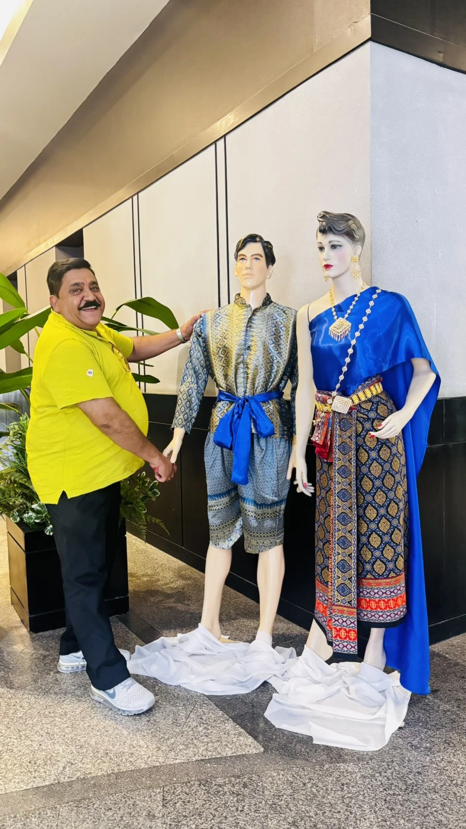 Smiling visitor posing beside mannequins dressed in colorful traditional Thai clothing in Phuket
