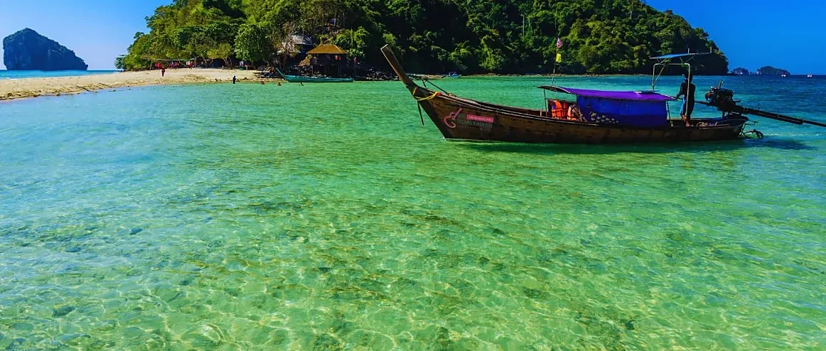 Wooden longtail boat gliding past limestone islands at sunset in Krabi with golden light reflecting on calm water