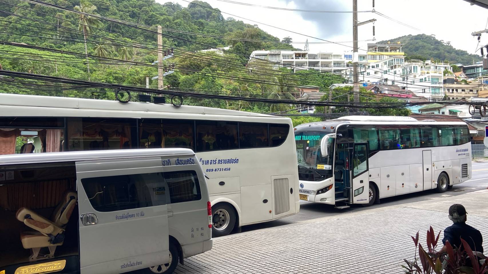 Tour buses and passenger van parked on a tropical hillside street in Phuket
