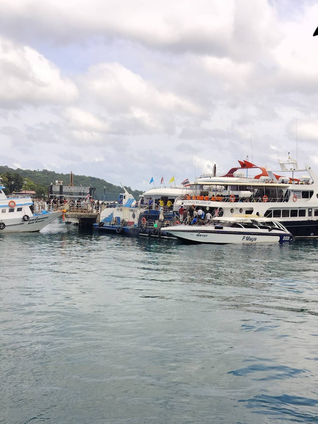 Ferry and speedboats boarding passengers at a Phuket pier under a cloudy sky