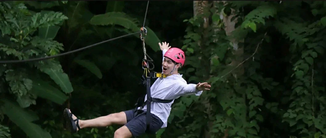 Traveler ziplining through lush rainforest at Hanuman World adventure park in Phuket