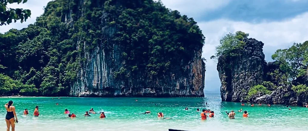 Speed boat anchored near Hong Island's turquoise lagoon surrounded by towering limestone cliffs, Krabi