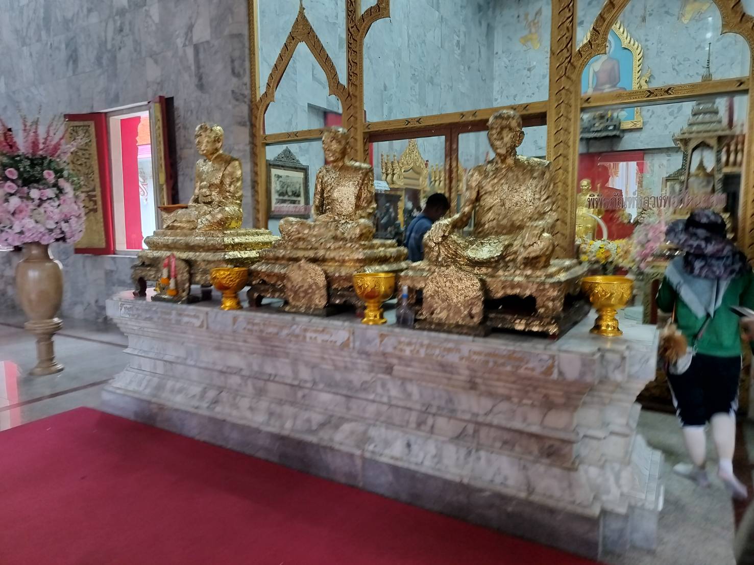 Gold-leaf monk statues and floral offerings inside a Buddhist temple in Phuket
